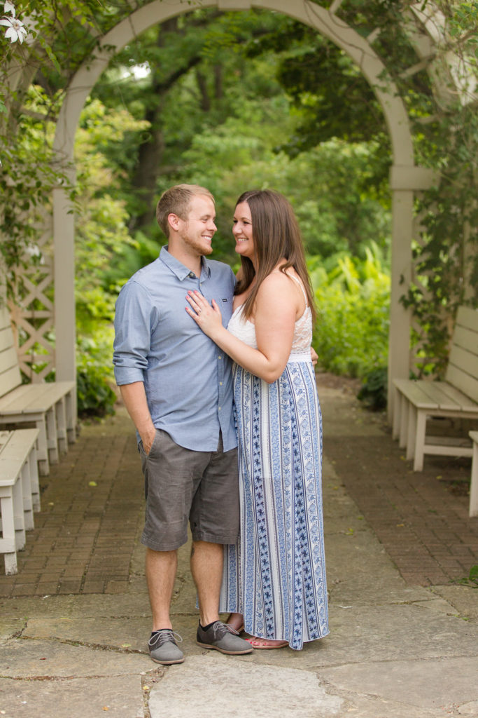engagement photo under a white arbor with vines