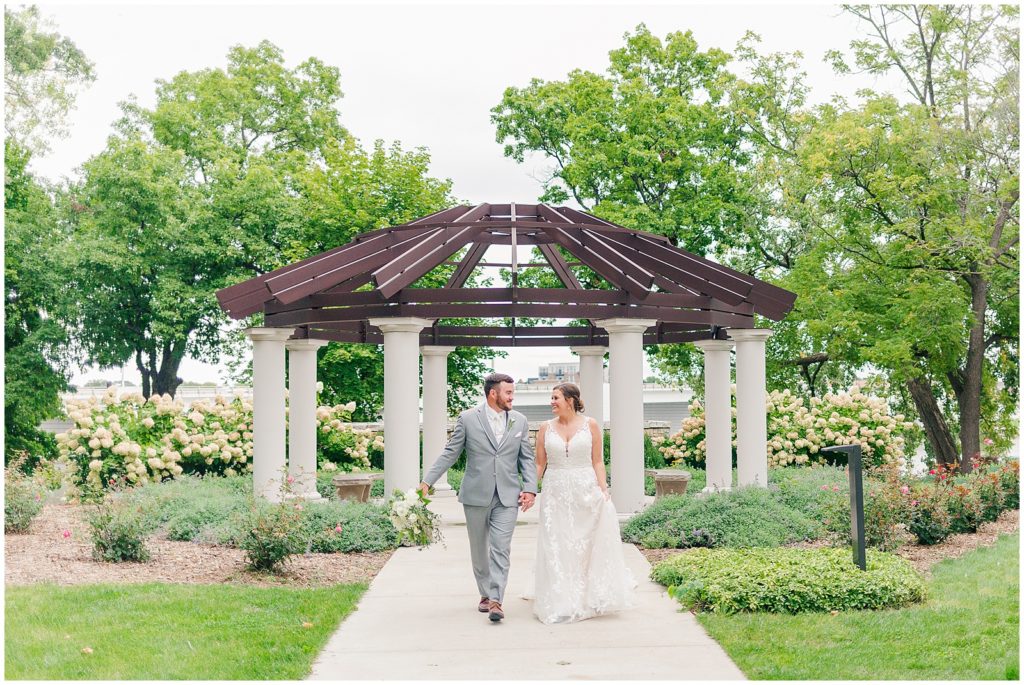 bride and groom walk down path on campus of st. norbert's college 
