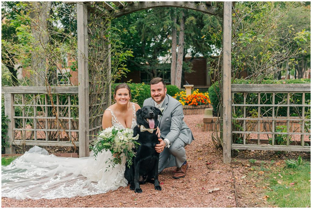 bride and groom crouch next to their black lab 
