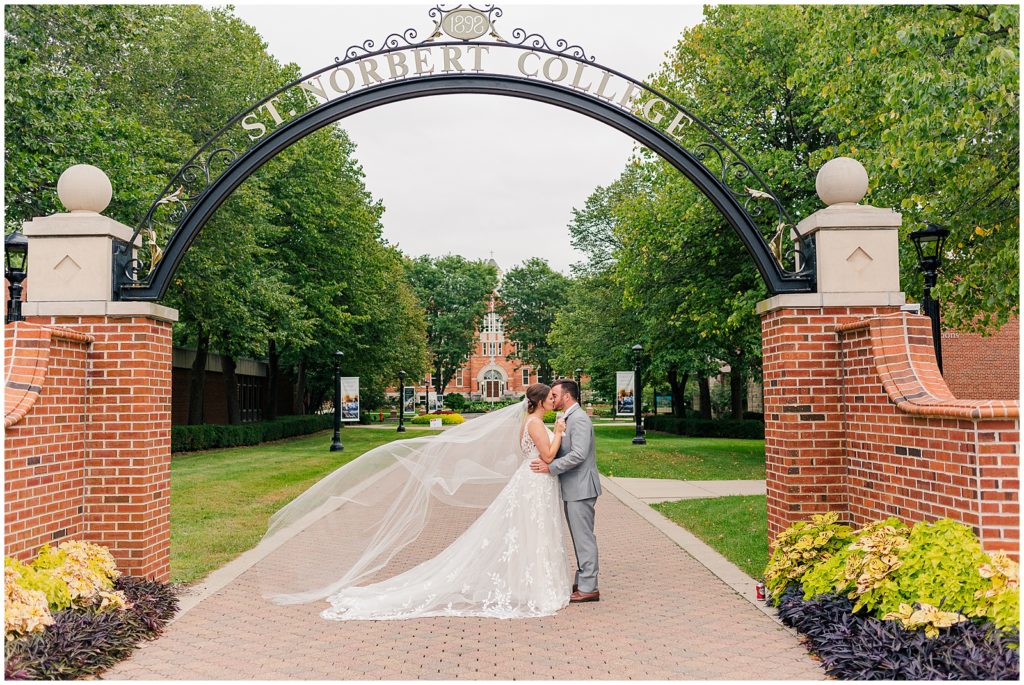 bride and groom portrait with veil flowing under the st. norbert college sign 