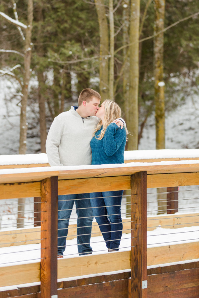 engagement photo bridge blue sweater snow and pine trees 