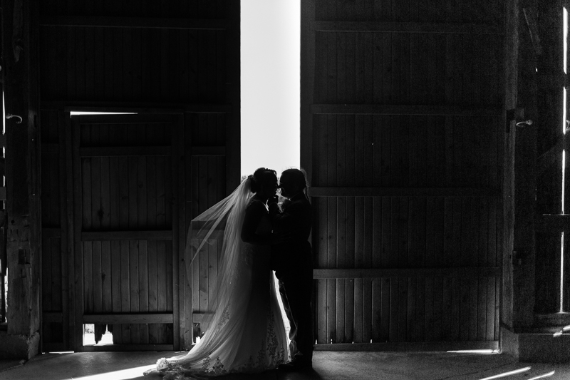black and white moody photo of bride and groom standing in barn doors about thyme farm 